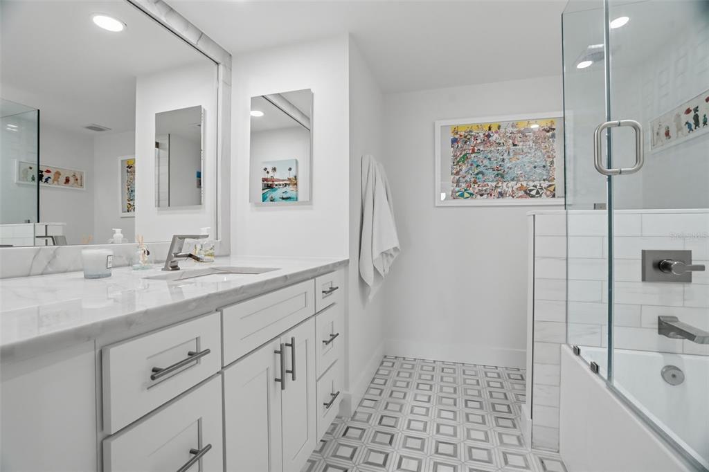 A modern bathroom features a white vanity, marble countertop, patterned tile floor, and glass shower — 6 BELLEVIEW BOULEVARD UNIT 705, BELLEAIR, FL