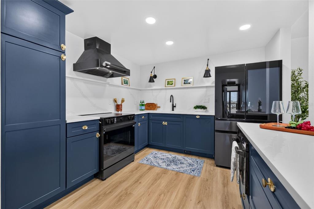 A kitchen features blue cabinets, white countertops, a black range hood, and light wood flooring — 855 BAYWAY BOULEVARD UNIT 503, CLEARWATER, FL