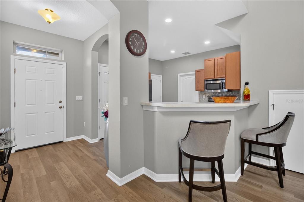 A kitchen with a breakfast bar and two chairs overlooks an entryway with wood flooring — 2169 BROADWAY VIEW AVENUE, BRANDON, FL