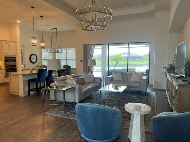 An open-concept living room features a large chandelier, gray sofa, and blue accent chairs — 5528 ARNIE LOOP, LAKEWOOD RANCH, FL