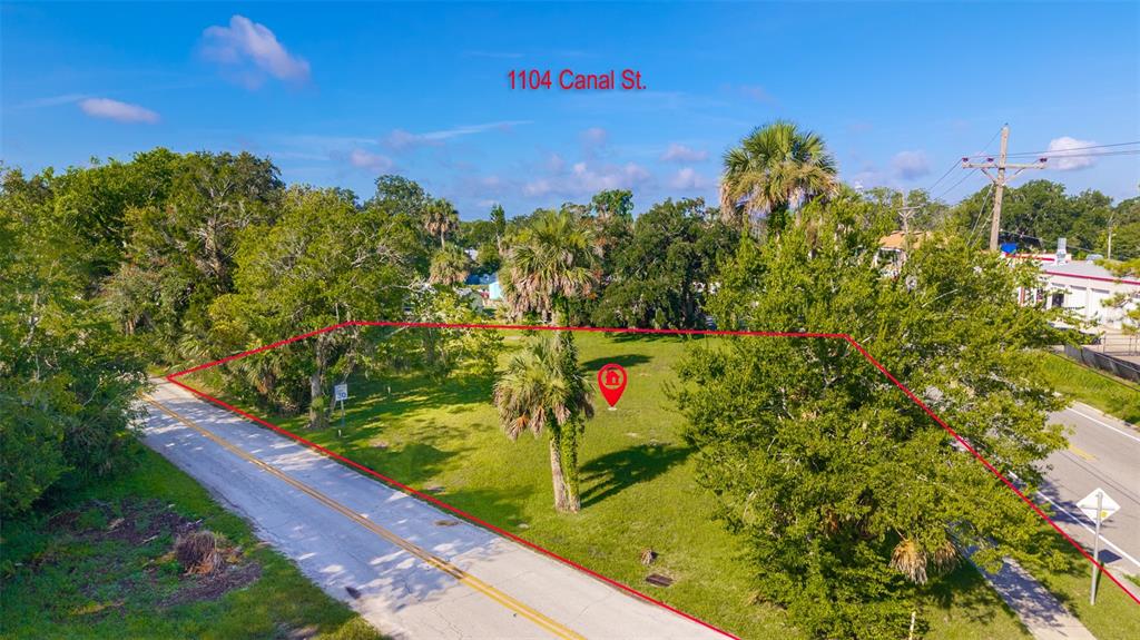 An aerial view shows a vacant, grassy lot outlined in red between two paved roads — 1104 CANAL STREET, NEW SMYRNA BEACH, FL