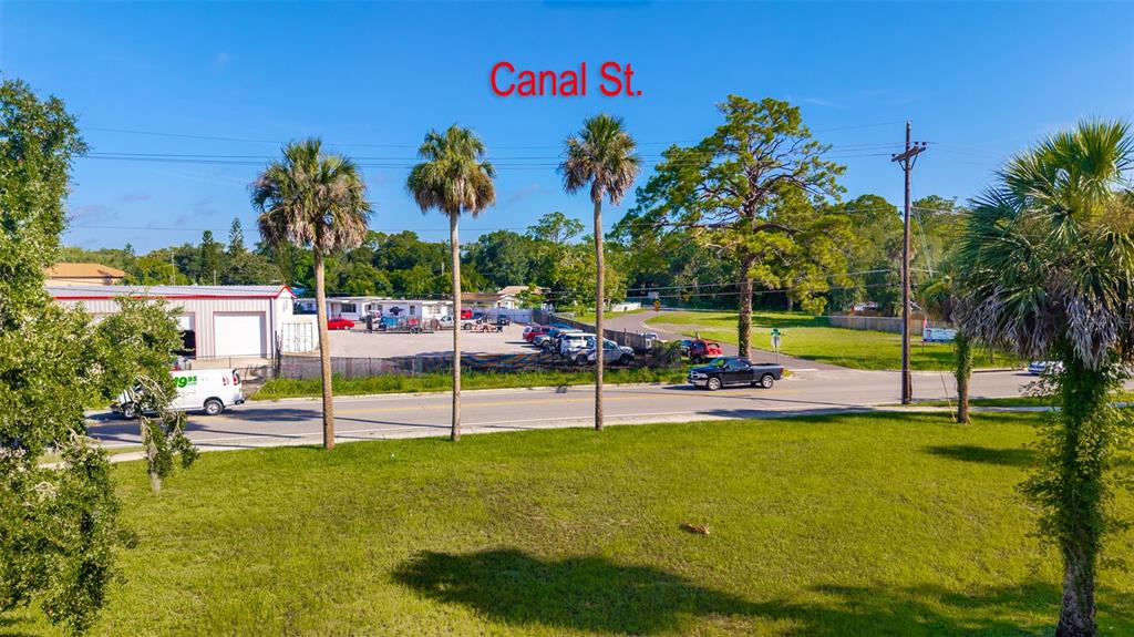 An elevated view shows a grassy lot bordering a road with palm trees and buildings — 1104 CANAL STREET, NEW SMYRNA BEACH, FL