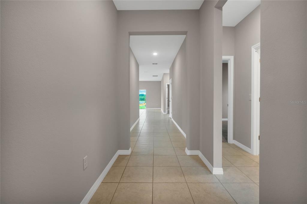A long, tiled hallway with grey walls leads toward a window with a green view — 717 CROWN ROSE DRIVE, EAGLE LAKE, FL