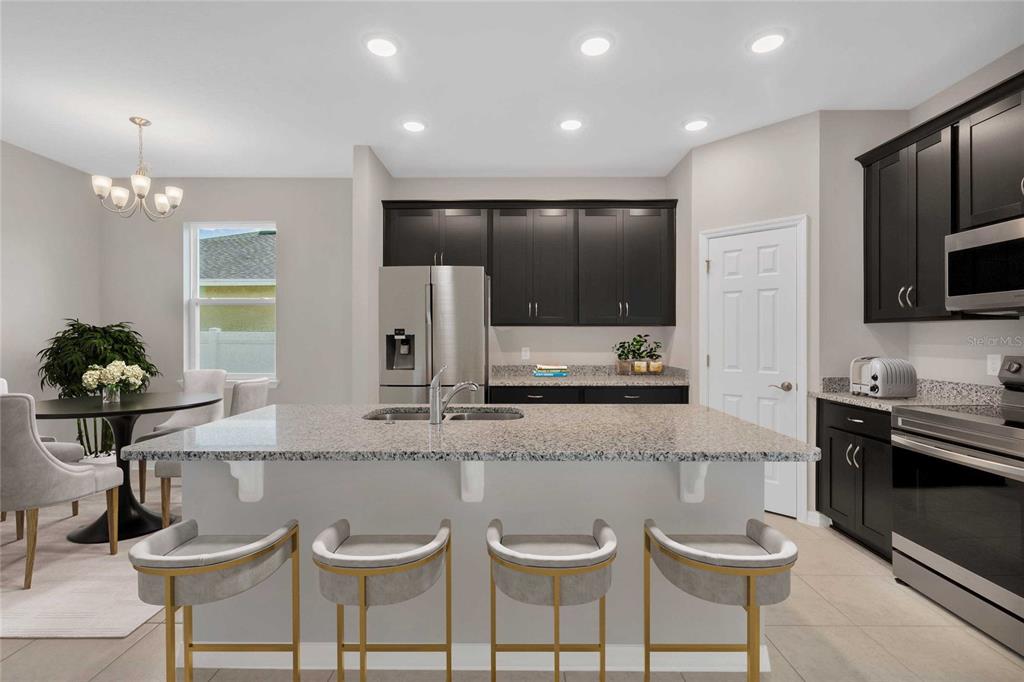 A modern kitchen features dark cabinetry, granite countertops, a central island, and stainless steel appliances — 717 CROWN ROSE DRIVE, EAGLE LAKE, FL