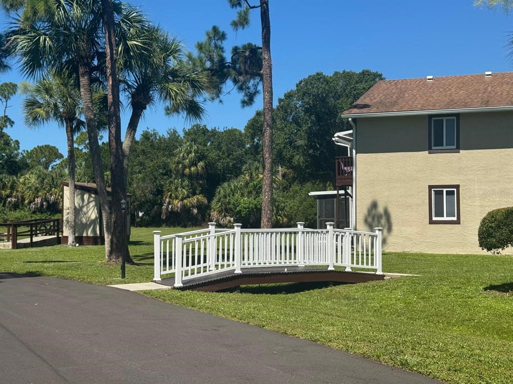A small white arched footbridge sits on a grassy lawn next to a tan building — 22481 WESTCHESTER BOULEVARD UNIT B36, PORT CHARLOTTE, FL