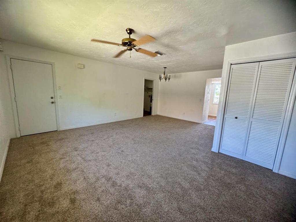 A carpeted living room features a ceiling fan, white walls, and a louvered closet door — 22481 WESTCHESTER BOULEVARD UNIT B36, PORT CHARLOTTE, FL