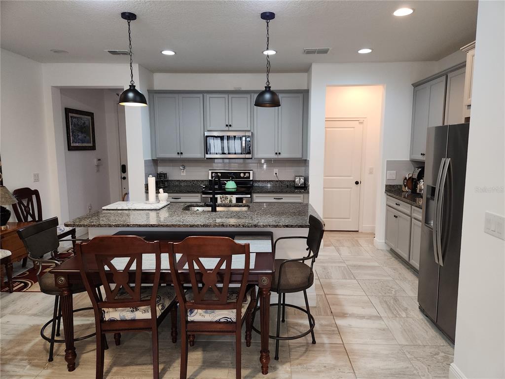 A kitchen features gray cabinets, granite countertops, a central island, and a dining table — 5508 VIOLA LEE WAY, LUTZ, FL