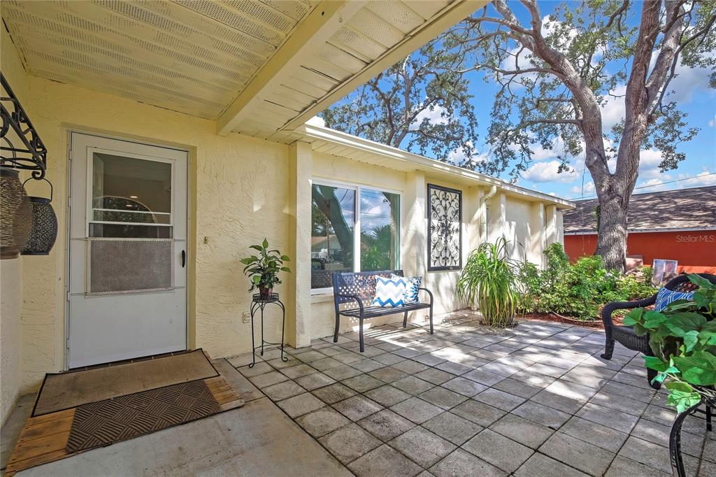 A paved patio sits in front of a yellow house with a white door — 1185 MACFARLANE AVENUE, SPRING HILL, FL