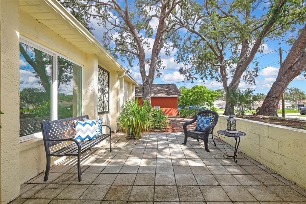 A paved patio features a metal bench, a wicker chair, and a small side table — 1185 MACFARLANE AVENUE, SPRING HILL, FL