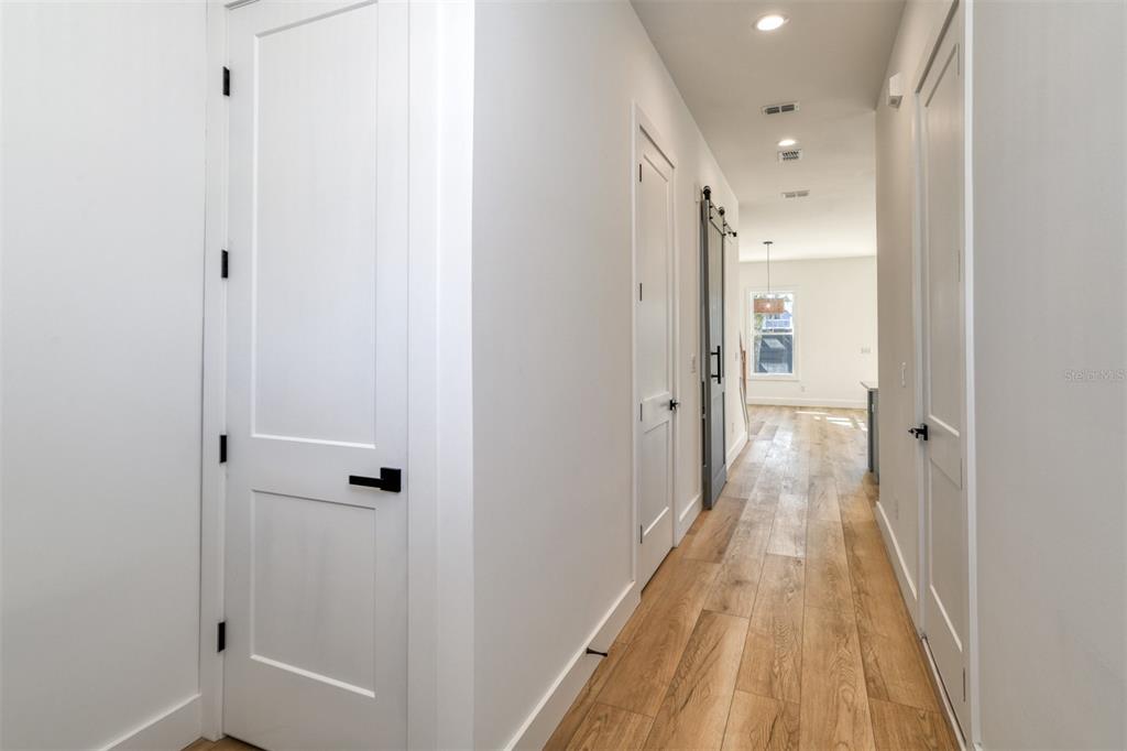 A hallway with light wood flooring leads toward a bright room with a barn door — 7 SEBASTIAN AVENUE UNIT D, ST AUGUSTINE, FL