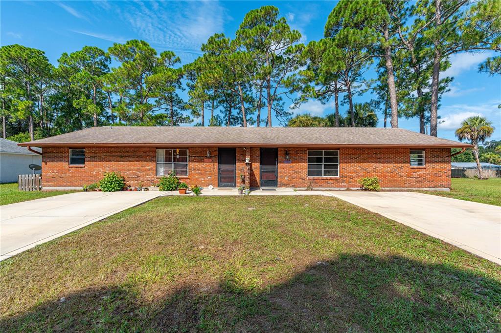 A single-story brick duplex with two front doors, concrete driveways, and surrounding pine trees — 2304 INDIA PALM DRIVE, EDGEWATER, FL