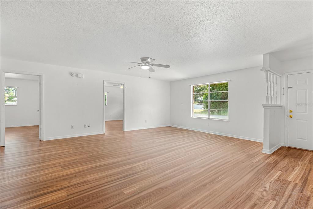 An empty living room features light wood-look flooring, white walls, and a ceiling fan — 2304 INDIA PALM DRIVE, EDGEWATER, FL