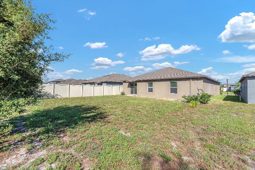 The backyard of a single-story house features a tan stucco exterior and vinyl fencing — 5518 BLUE AZURE DRIVE, WIMAUMA, FL