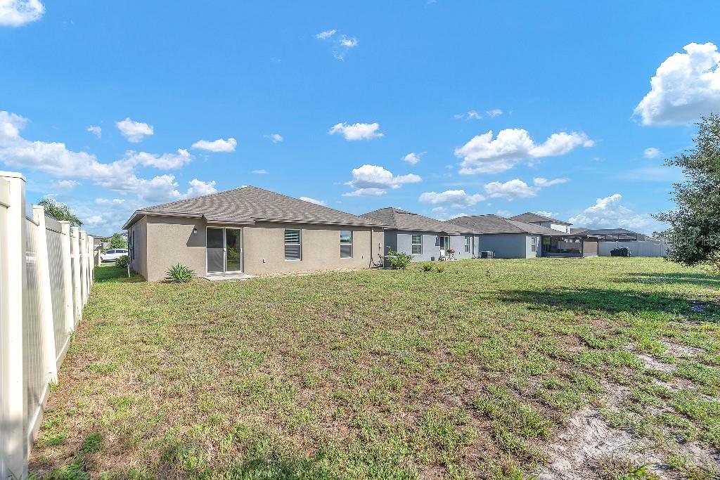 The backyard of a single-story house features a sliding glass door and a vinyl fence — 5518 BLUE AZURE DRIVE, WIMAUMA, FL
