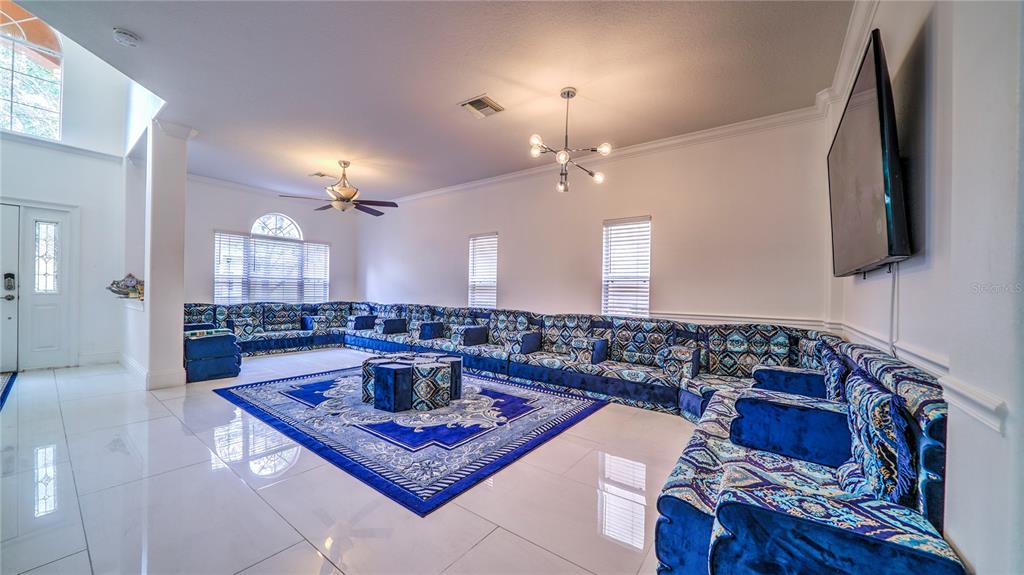 A spacious living room features white tile floors, blue patterned sectional seating, and a large rug — 6956 LUCCA STREET, ORLANDO, FL