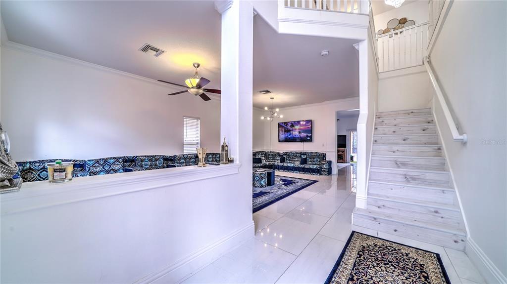 A bright foyer features white tile floors, a staircase, and an open view into living areas — 6956 LUCCA STREET, ORLANDO, FL