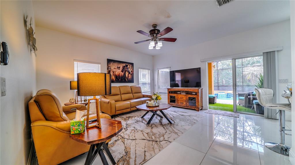 A living room features tan leather furniture, a marble-patterned rug, and sliding glass patio doors — 6956 LUCCA STREET, ORLANDO, FL