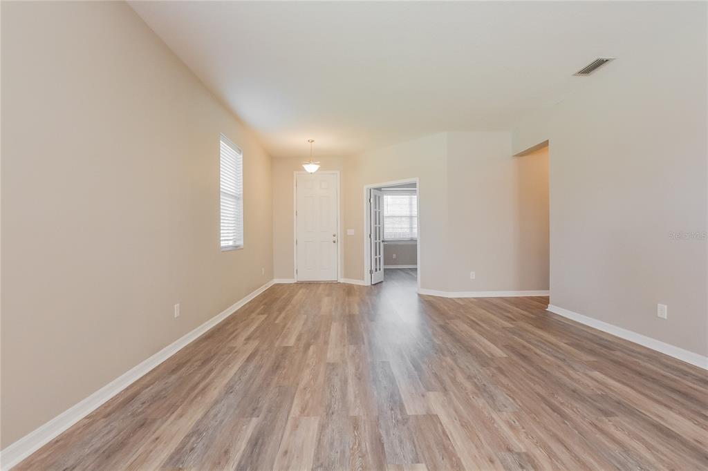 An empty room with light-colored walls and wood-look flooring features a white door and entryway — 5061 GANDROSS LANE, MOUNT DORA, FL