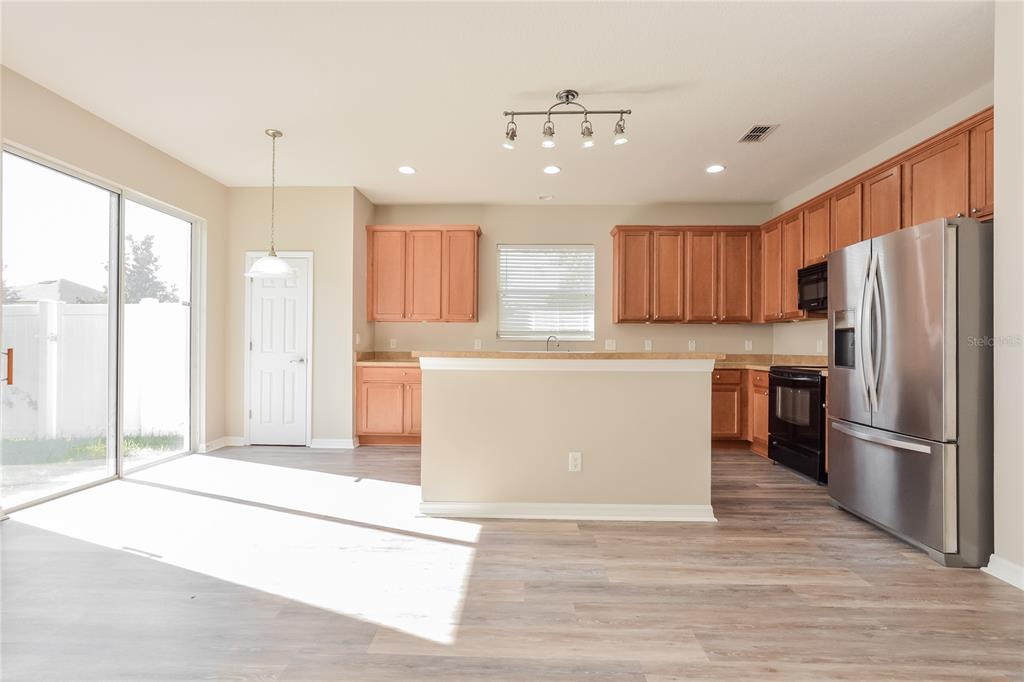 A kitchen with wood cabinets, stainless steel appliances, and an island opens to a patio — 5061 GANDROSS LANE, MOUNT DORA, FL