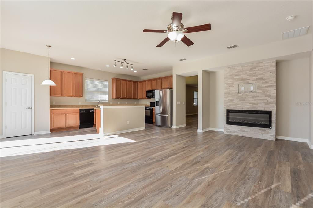 An open-concept living area features wood-look flooring, a kitchen with wood cabinets, and a fireplace — 5061 GANDROSS LANE, MOUNT DORA, FL