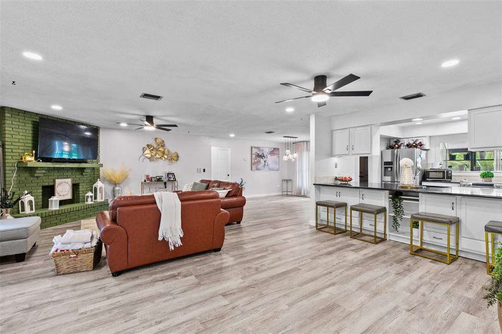 A living room with a green brick fireplace opens into a kitchen with white cabinets — 10611 DEERGRASS LANE, ORLANDO, FL