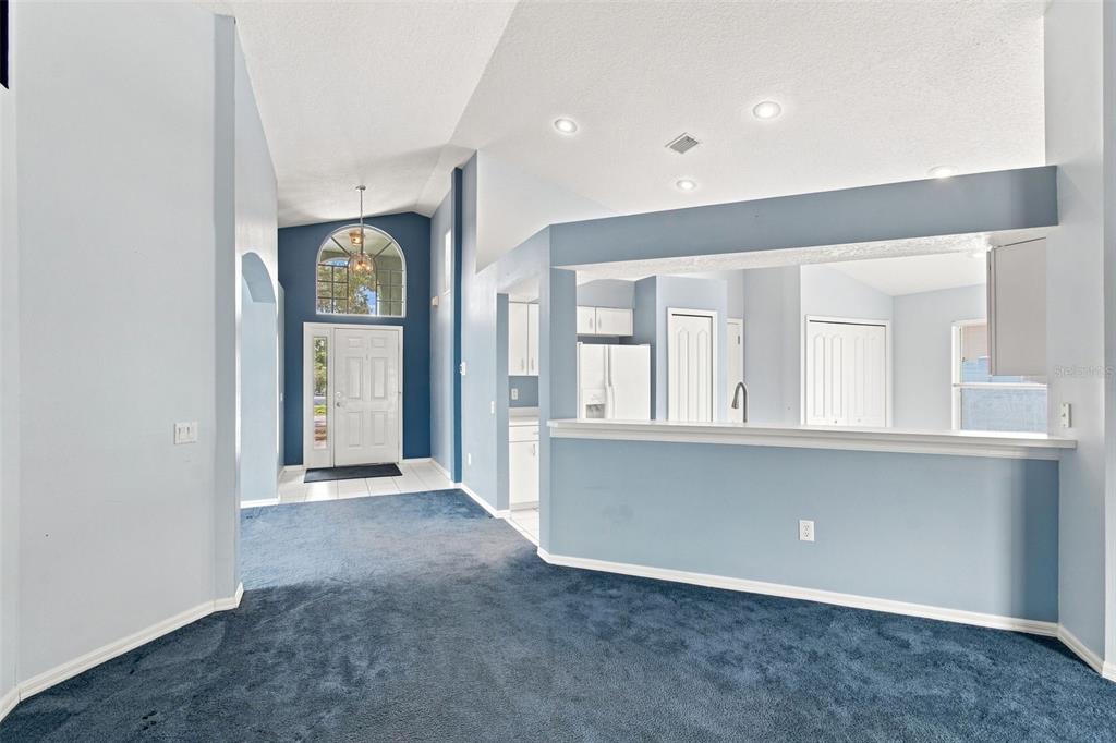 A living area with blue carpet leads to an entryway with a vaulted ceiling — 3838 BELLEWATER BLVD, RIVERVIEW, FL