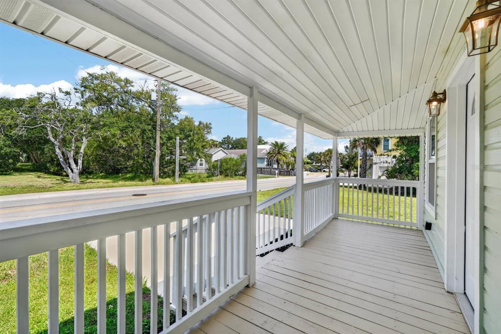 A covered wooden porch with white railings overlooks a road and trees — 255 RIBERIA STREET, ST AUGUSTINE, FL