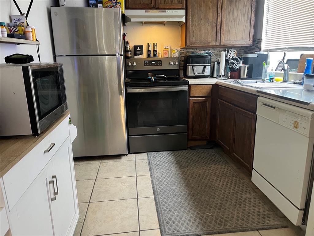 A kitchen features stainless steel appliances, dark wood cabinets, white lower cabinets, and tile flooring — 12506 FOX CROFT LANE, HUDSON, FL
