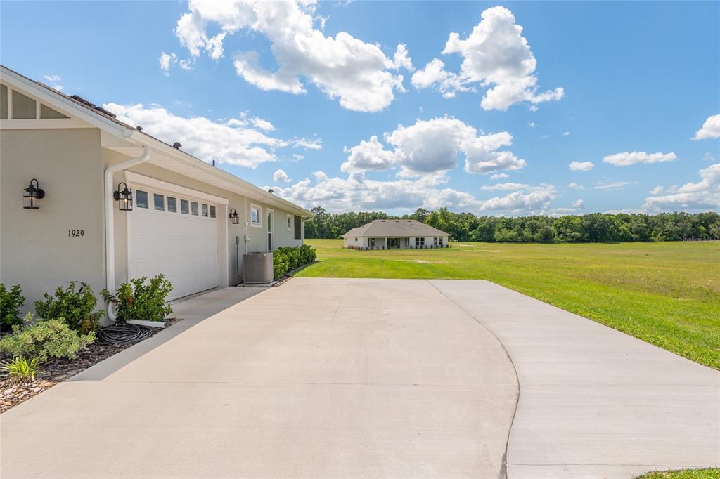 A concrete driveway leads toward the side of a house with a white garage door — 1929 NW 85TH LOOP, OCALA, FL