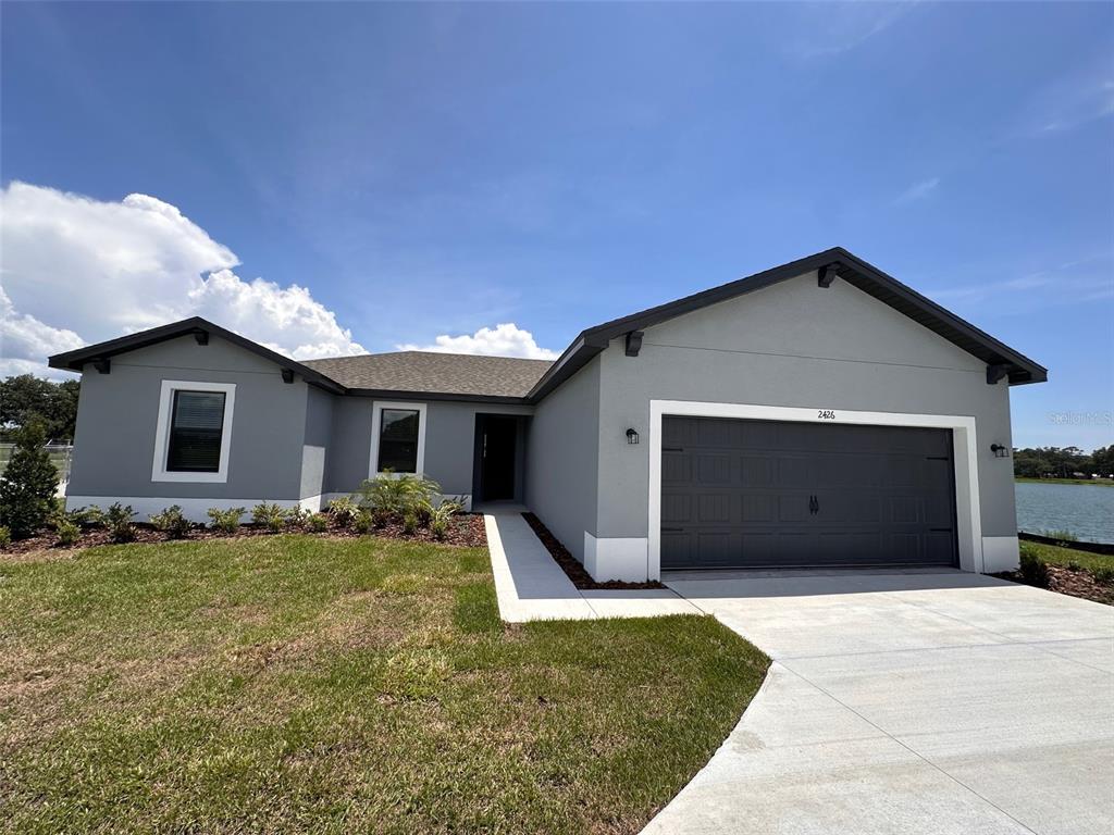 A single-story gray house with a two-car garage and a concrete driveway faces a lake — 2426 HIERS ROAD, DOVER, FL