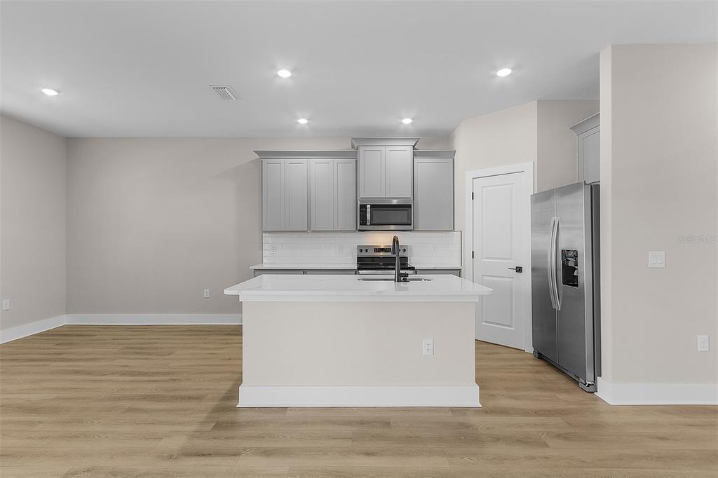 A kitchen features gray cabinets, a white island, stainless steel appliances, and light wood flooring — 2426 HIERS ROAD, DOVER, FL