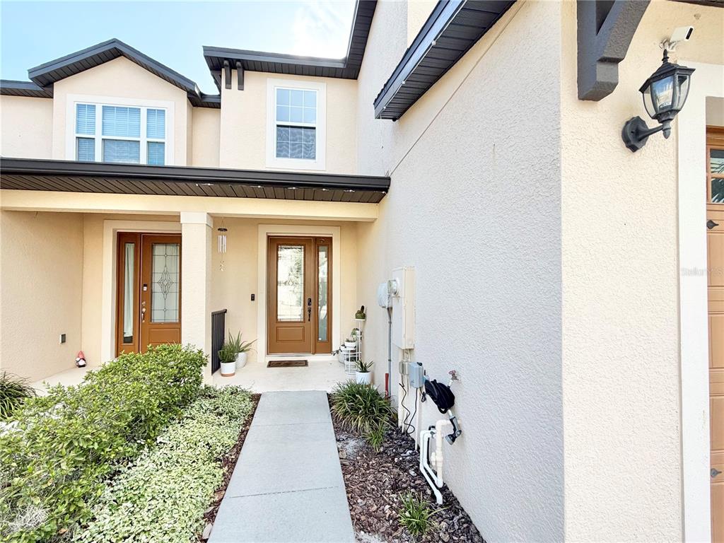 A concrete walkway leads to the front entrance of a two-story stucco house — 11287 CAY SPRUCE WAY, SAN ANTONIO, FL