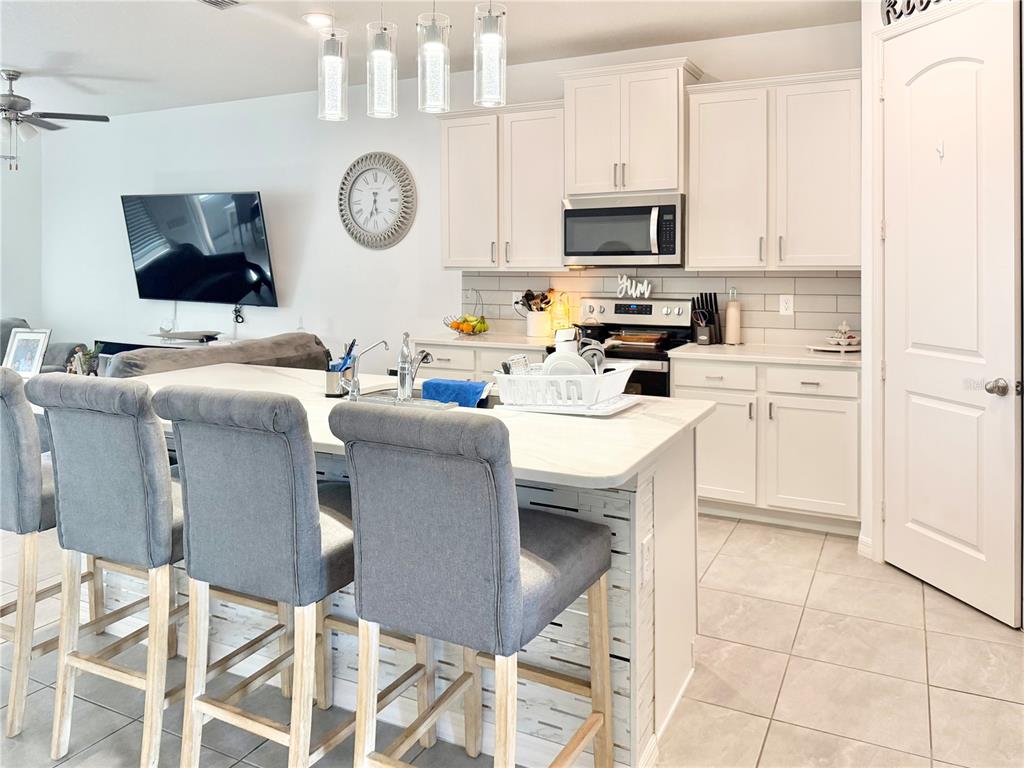 A kitchen features white cabinets, a central island with grey bar stools, and tile flooring — 11287 CAY SPRUCE WAY, SAN ANTONIO, FL