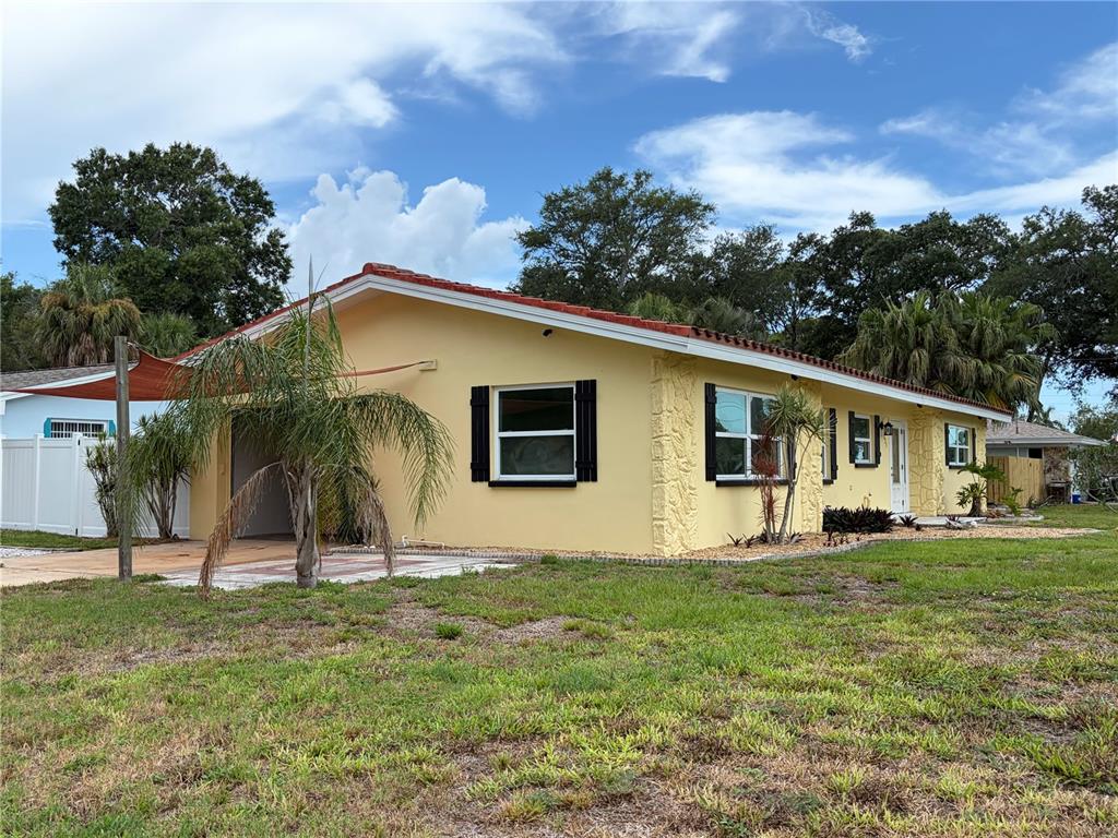 A yellow single-story house with a red tile roof and a carport under a shade sail — 623 PALM BOULEVARD, DUNEDIN, FL