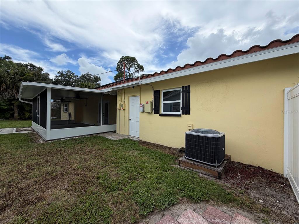 The exterior of a yellow house features a screened-in patio and an air conditioning unit — 623 PALM BOULEVARD, DUNEDIN, FL