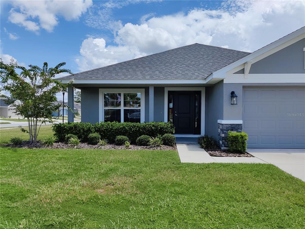 A gray single-story house features a dark front door, a garage, and a landscaped front yard — 5568 OCEAN BREEZE DRIVE, SPRING HILL, FL