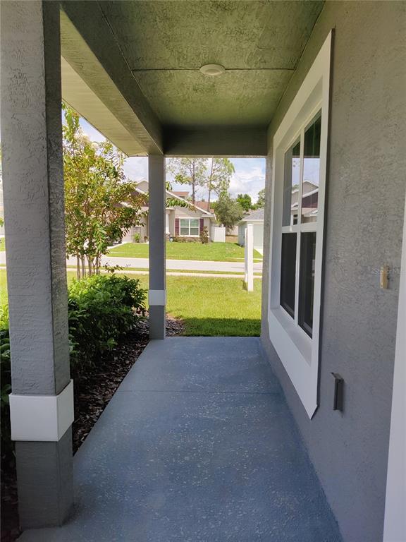 A covered concrete front porch features gray stucco walls, a support column, and a window — 5568 OCEAN BREEZE DRIVE, SPRING HILL, FL