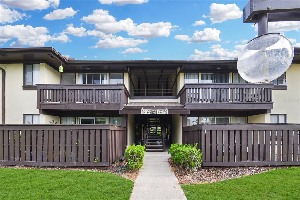 A two-story apartment building exterior features wooden balconies, a central staircase, and a grassy lawn — 40 CLUB HOUSE DRIVE UNIT 207, PALM COAST, FL