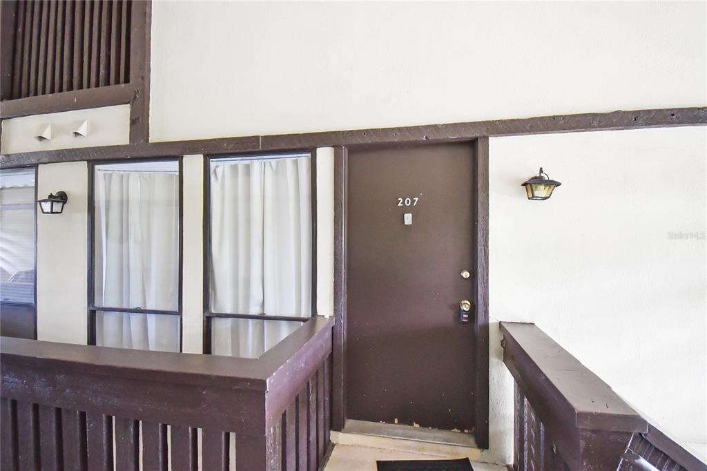 An exterior view of a brown apartment door labeled 207 with a wooden balcony railing — 40 CLUB HOUSE DRIVE UNIT 207, PALM COAST, FL