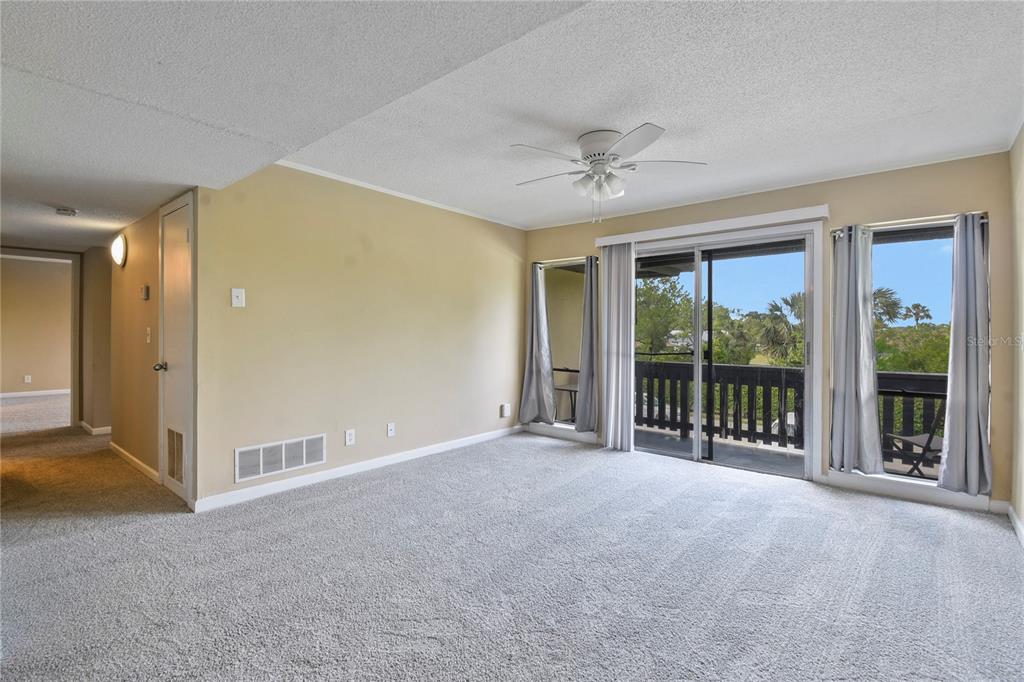 A living room with beige walls, gray carpeting, a ceiling fan, and a sliding glass door — 40 CLUB HOUSE DRIVE UNIT 207, PALM COAST, FL