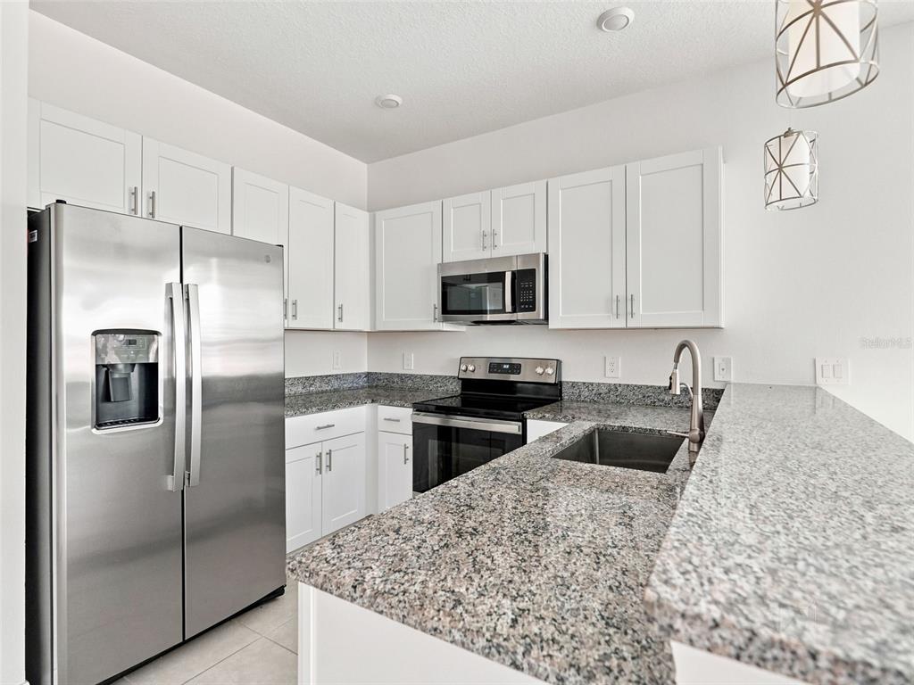 A kitchen features white cabinets, granite countertops, and stainless steel appliances — 10317 TRUMPET HONEYSUCKLE WAY, SAN ANTONIO, FL