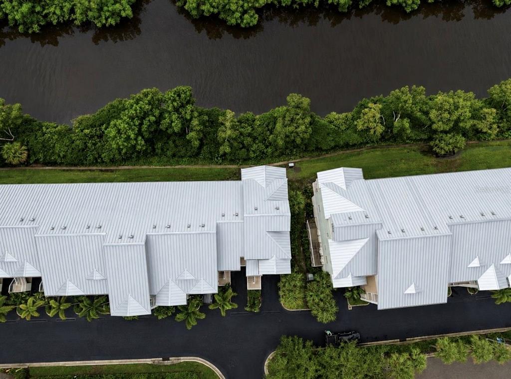 An aerial view shows two adjacent townhomes with metal roofs situated near a tree-lined waterway — 3228 MANGROVE POINT DRIVE, RUSKIN, FL