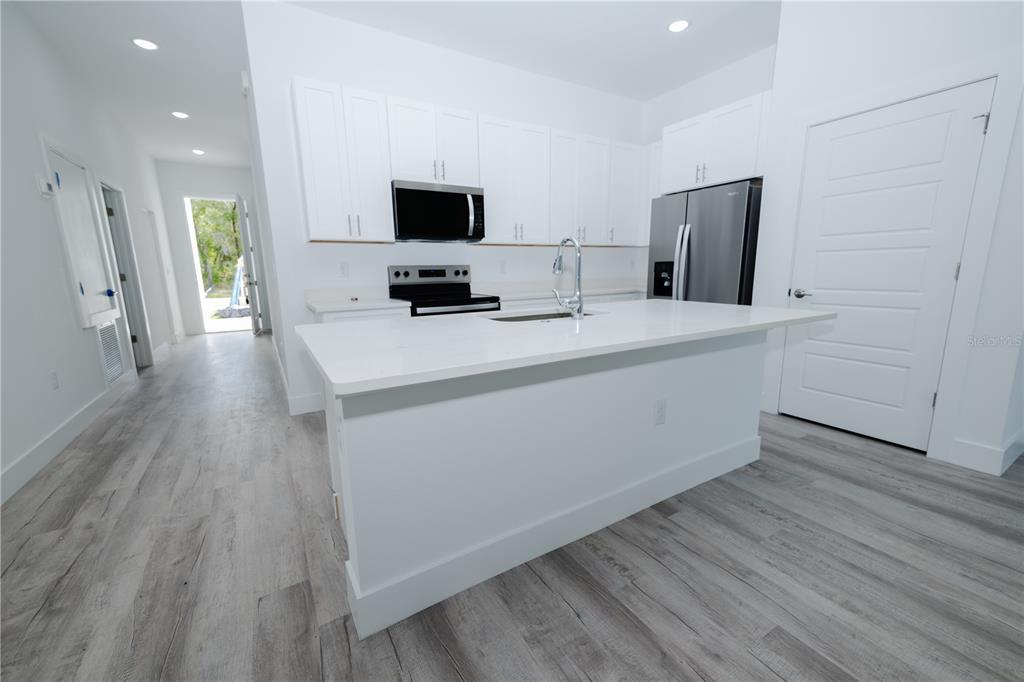 A modern kitchen features white cabinetry, stainless steel appliances, a central island, and wood-look flooring — 9298 N MENDOZA WAY, CITRUS SPRINGS, FL