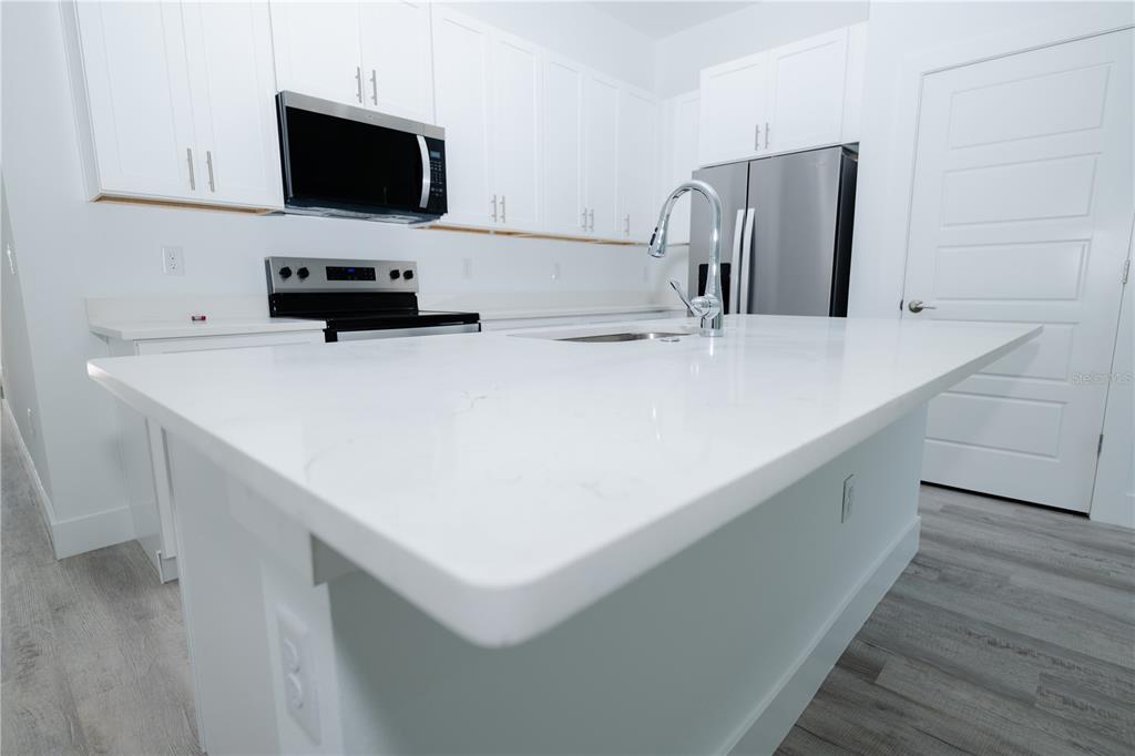 A modern kitchen features white cabinets, stainless steel appliances, a center island, and wood-look flooring — 9298 N MENDOZA WAY, CITRUS SPRINGS, FL