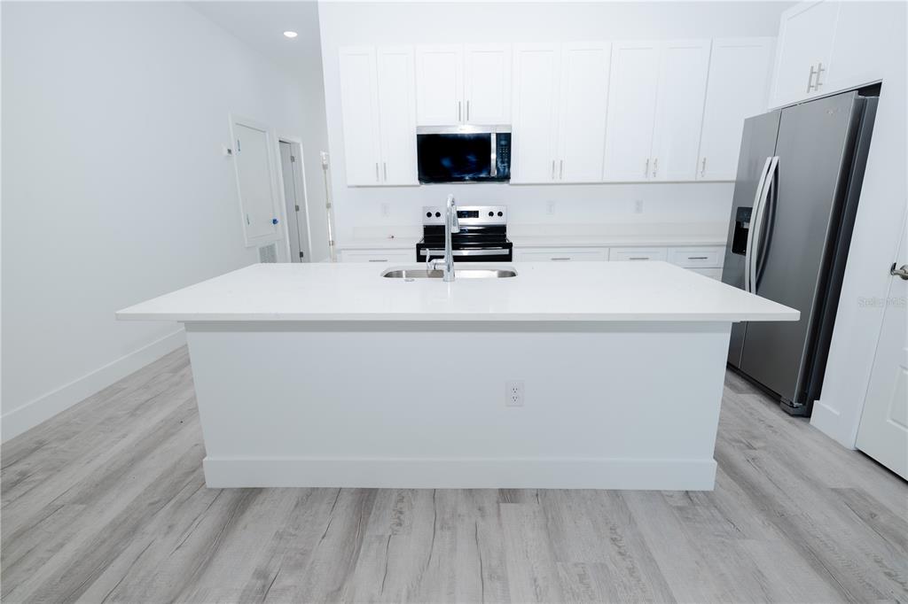 A modern kitchen features white cabinets, stainless steel appliances, and a large quartz-topped island — 9298 N MENDOZA WAY, CITRUS SPRINGS, FL
