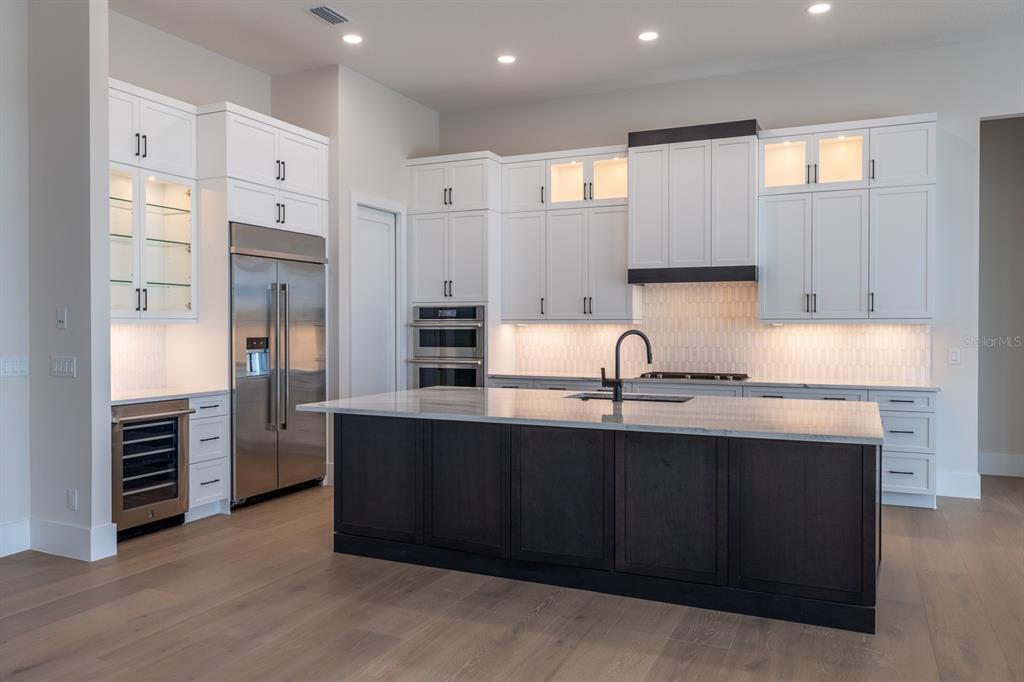 A modern kitchen features white cabinetry, a dark wood island, and stainless steel appliances — 1003 BLUE SHELL LOOP, SARASOTA, FL