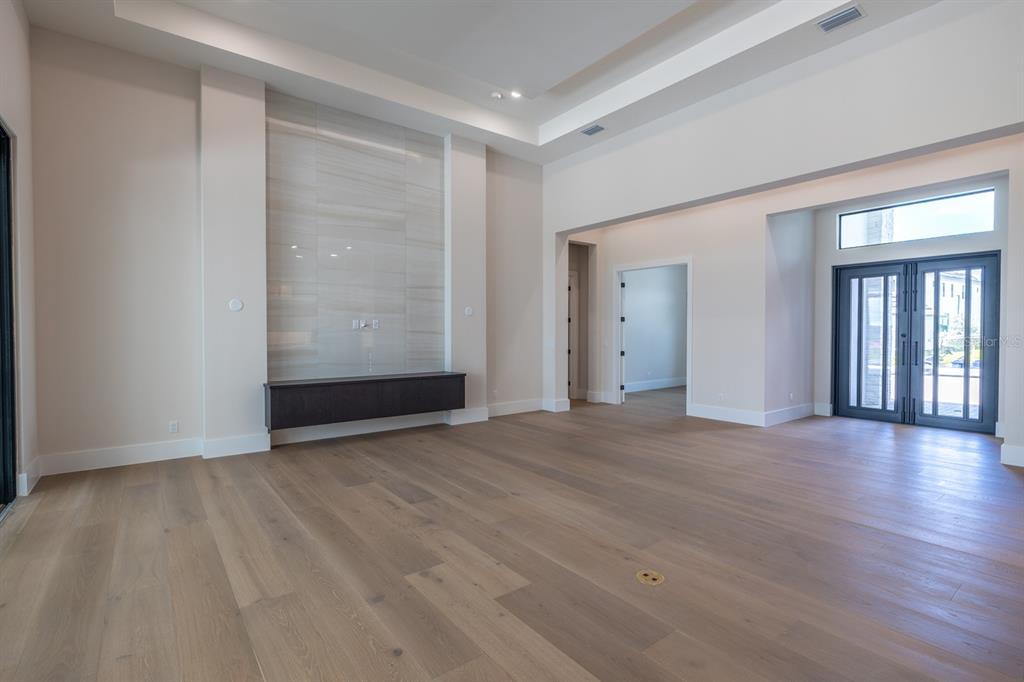 A spacious living room features light wood flooring, a tiled accent wall, and double glass doors — 1003 BLUE SHELL LOOP, SARASOTA, FL