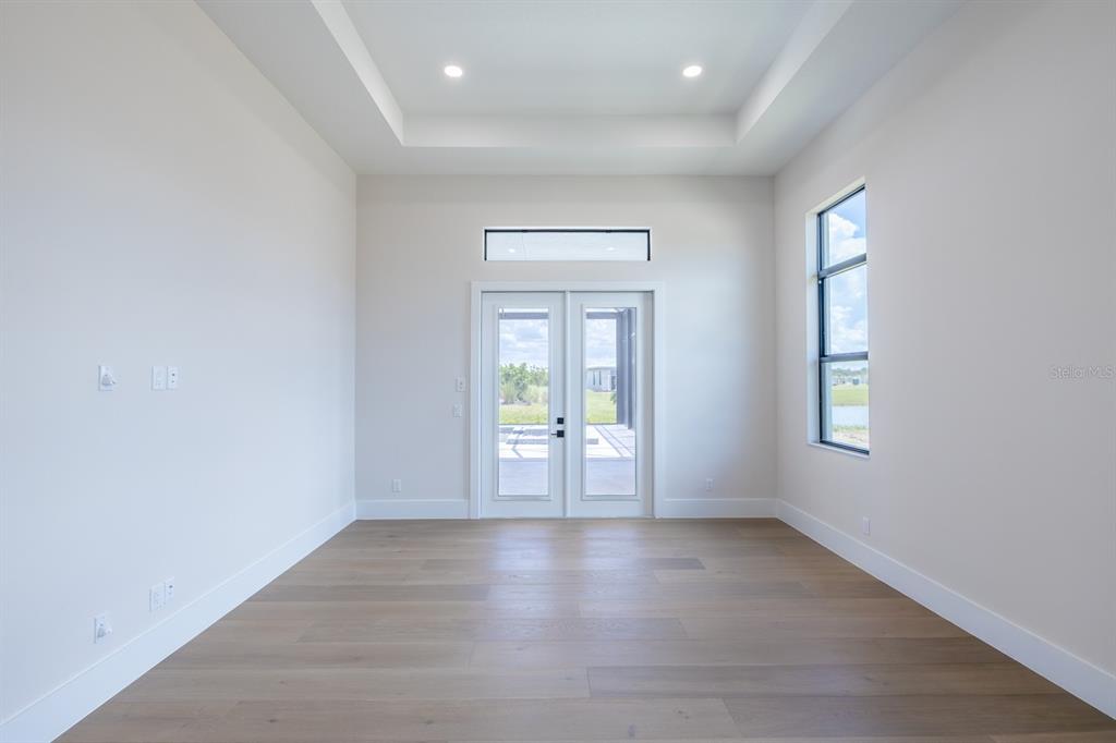 An empty room with light wood floors, a tray ceiling, and double glass doors — 1003 BLUE SHELL LOOP, SARASOTA, FL