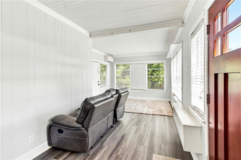 A sunroom features light wood-look flooring, white paneled walls, a gray reclining sofa, and large windows — 208 W 17TH STREET, SANFORD, FL