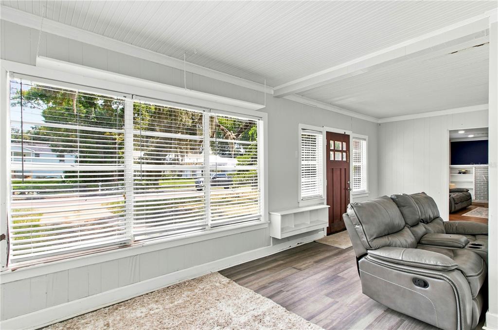 A sunroom with white paneled walls, large windows with blinds, and a gray reclining sofa — 208 W 17TH STREET, SANFORD, FL